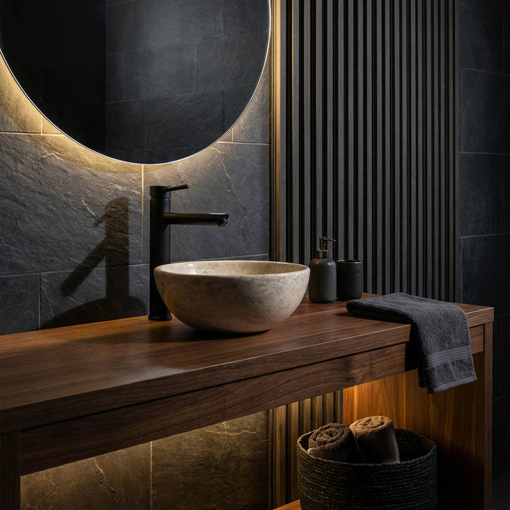 Round countertop washbasin made of light natural stone on a dark wooden washbasin with black fittings in an elegant bathroom ambience