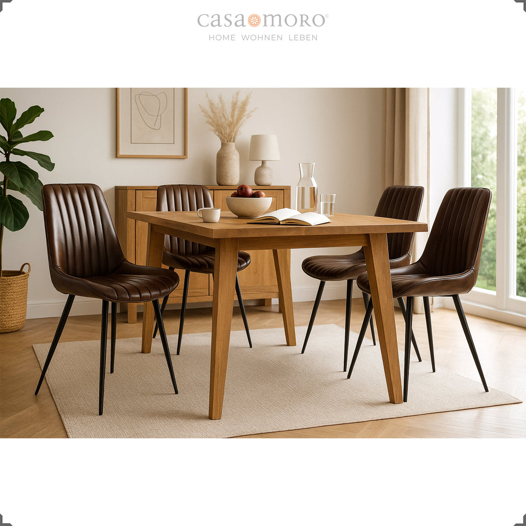 Four antique brown leather chairs with black painted metal legs at a rectangular wooden table in a bright kitchen with natural light