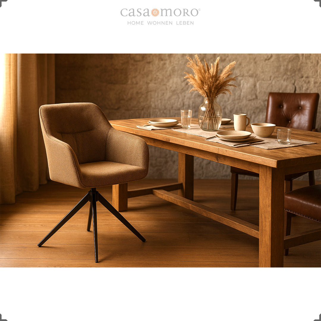 360° rotating upholstered chair with armrests in brown on a wooden table with a natural stone wall, a set table and warm light