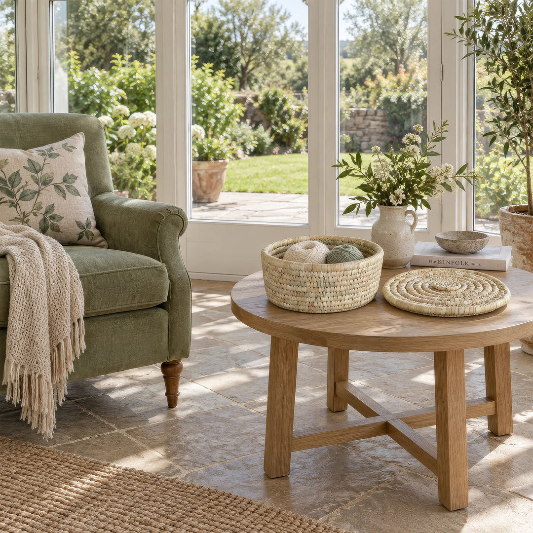 An open palm-leaf basket, 28 cm in diameter, containing balls of wool and with its lid set aside, sitting on a table in the sunroom.