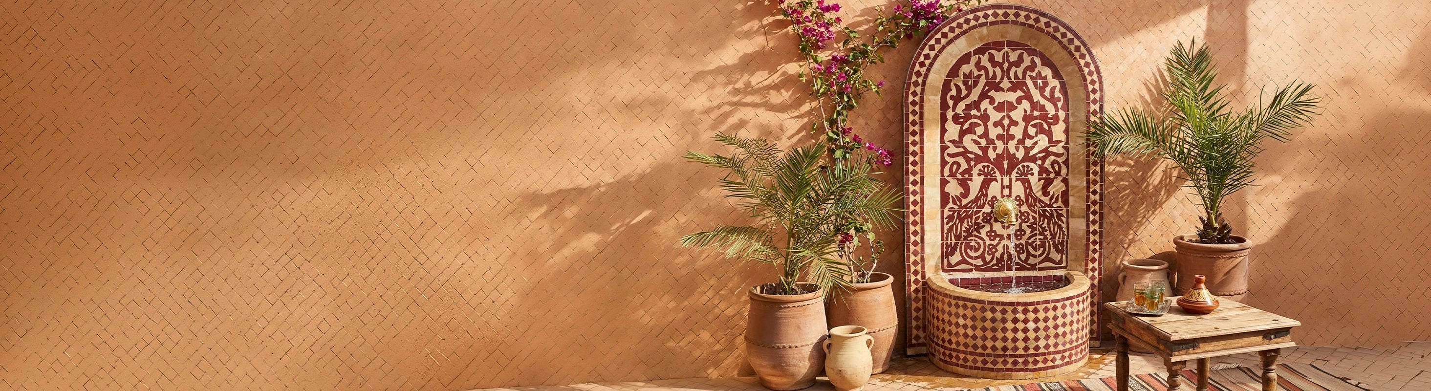 mosaic fountain – Marokkanischer Mosaikbrunnen mit Zellige-Fliesen als Wasserbrunnen im Garten vor warmer Wand mit Pflanzen und orientalischer Atmosphäre