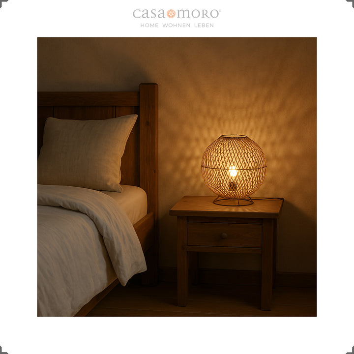 Round rattan bedside lamp on wooden table next to bed, warm light and cozy atmosphere