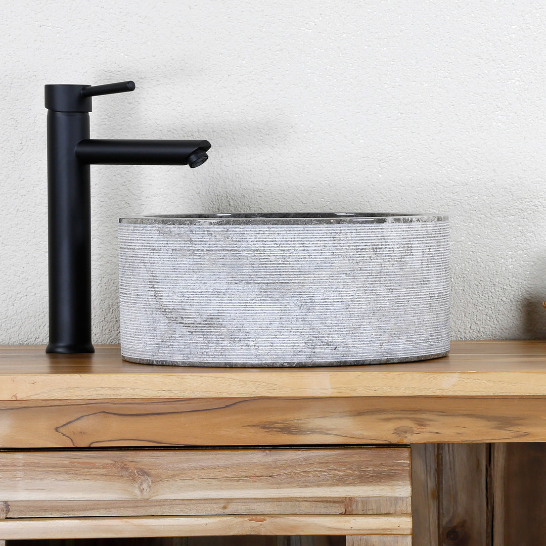 Modern Washbasin Made of light natural stone with a fine line structure and black fittings on a wooden console.