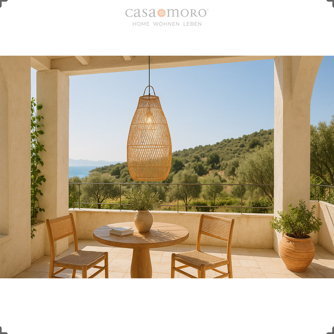 Large rattan lamp above a round dining table on a terrace with a view of the greenery and a Mediterranean atmosphere