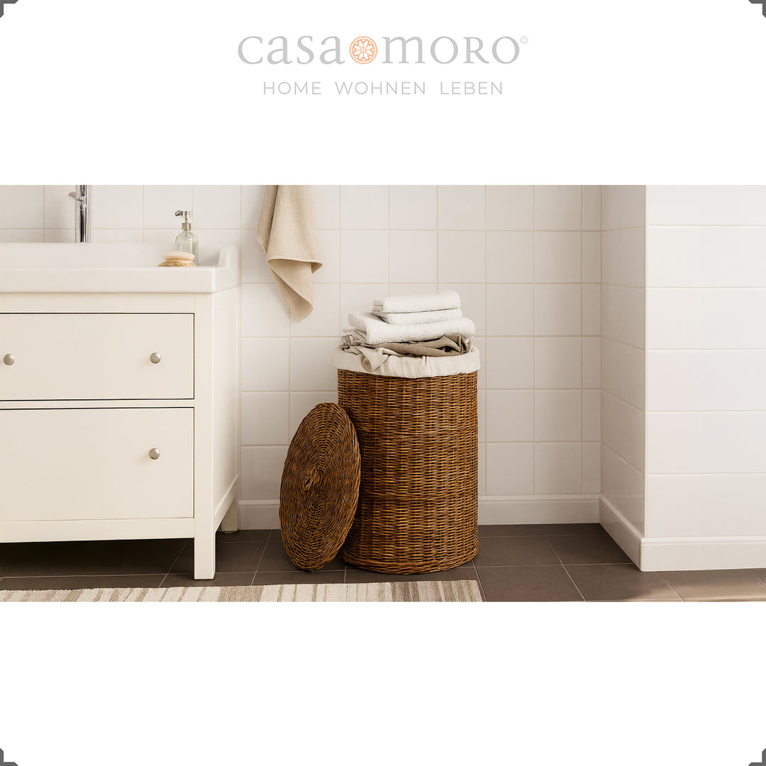 Dark brown rattan laundry basket with lid and inner bag in a light bathroom setting, decorated with towels