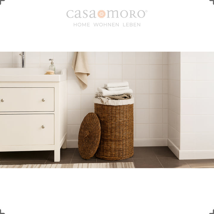 Dark brown rattan laundry basket with lid and inner bag in a light bathroom setting, decorated with towels