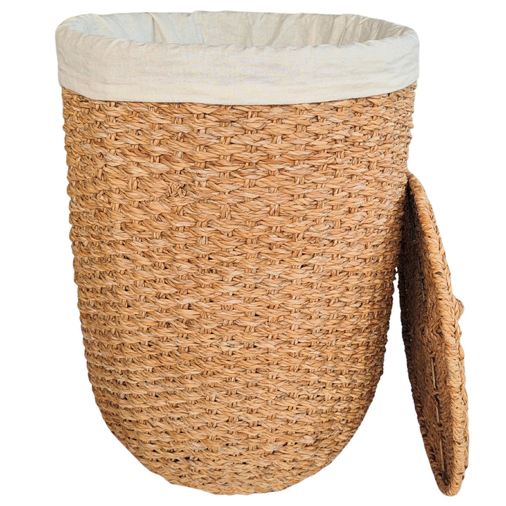 An open laundry basket made of natural-colored seagrass with a light-colored fabric insert and a lid that rests against the side.