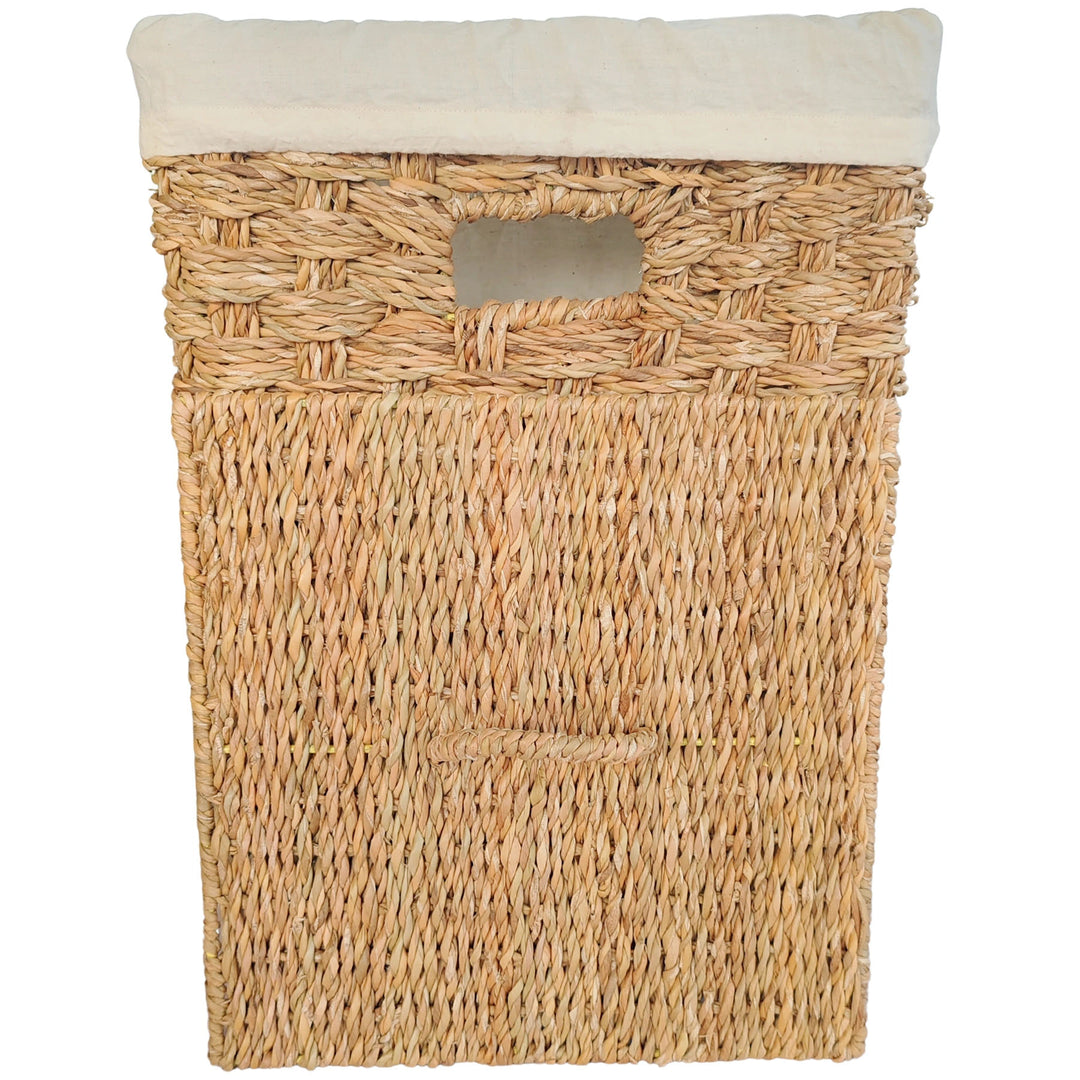 Square laundry basket made of seagrass with a light-colored fabric insert and a removable lid that rests against the front of the basket.