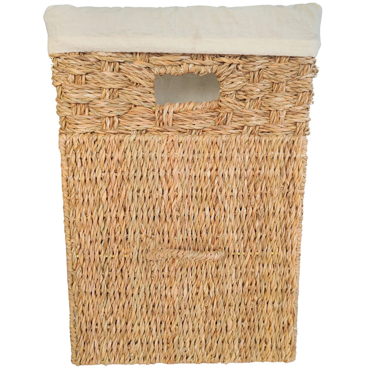 Square laundry basket made of seagrass with a light-colored fabric insert and a removable lid that rests against the front of the basket.