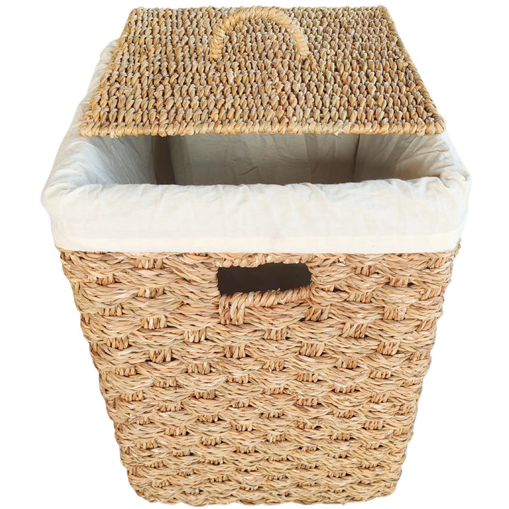 Square laundry basket made of seagrass with a raised lid, a light-colored fabric insert, and a handle opening.