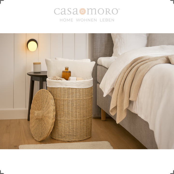 Round rattan laundry basket with lid in the bedroom, filled with pillows, blankets and toiletries