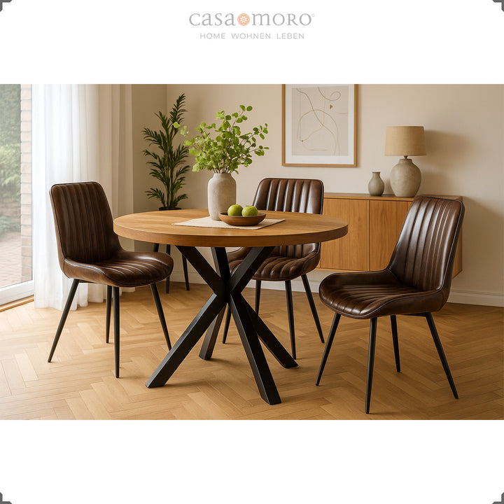 Three antique brown leather chairs with black painted metal legs at a round wooden table in the bright living room with parquet floors